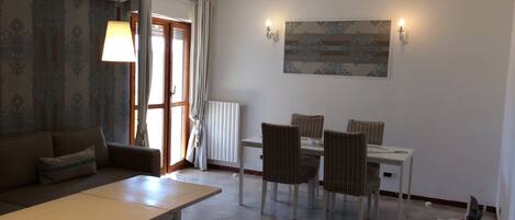 A dining area with a table and chairs, a sofa, a TV, and a painting on the wall.