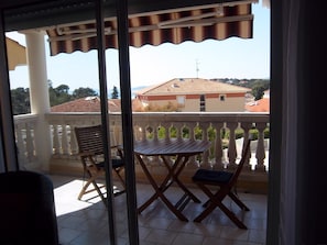 A balcony with a table and chairs, a white railing, and a view of buildings in the background.