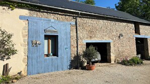 Un bâtiment rustique en pierre, avec une porte bleue portant l’inscription « LA PETITE FUGUE », une petite fenêtre et une allée gravillonnée.