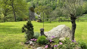 Un jardin avec un grand rocher, un petit arbre et une statue d’oiseau.