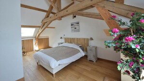 Une chambre avec un plafond en pente, des poutres en bois, un lit, des tables de chevet et une plante en pot.