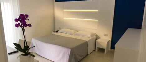 Un dormitorio moderno con cama, mesitas de noche, una orquídea en maceta y un control remoto en el suelo.
