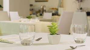 Una mesa dispuesta con dos vasos de cristal, una pequeña planta en maceta y cubiertos.