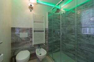 Un baño moderno con cabina de ducha de vidrio, un bidé y un perchero para toallas.
