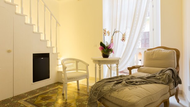 A room with a bed, a chair, a small table with a vase, a staircase, and a window with curtains. - Suite Le Perle (Taranto)