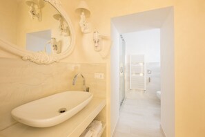 A modern bathroom with a large oval sink, a mirror with ornate detailing, and a shower area visible through an open door.