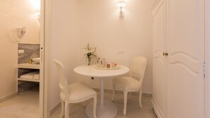 A small, white-walled room with a round table and two chairs, a white door, and a wall-mounted light fixture. - Suite Le Perle (Taranto)