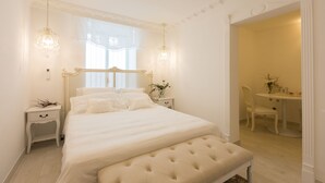 A bedroom with a large bed, bedside tables, a bench, a chair, and a small table with a plant. - Suite Le Perle (Taranto)