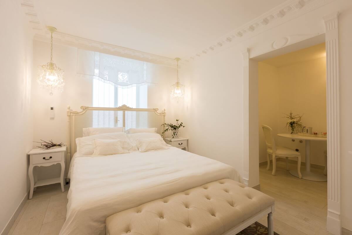 Ein Schlafzimmer mit einem großen Bett, Nachttischen, einer Bank, einem Sessel und einem kleinen Tisch mit einer Pflanze.
