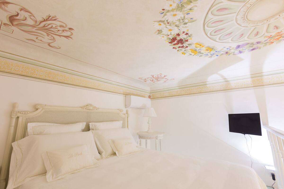 Ein Schlafzimmer mit einem Bett, Kissen, einem Nachttisch, einer Lampe und einem Fernseher.
