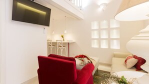 A modern living room with a red armchair, a sofa, a TV mounted on the wall, and a dining area with a table and chairs. - Suite Le Perle (Taranto)