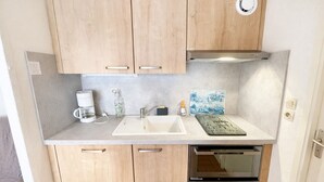 A compact kitchen with wooden cabinets, a built-in oven, a coffee maker, and a decorative tile backsplash. - Cozy Vacation Home Near Beach with Private Garden and Parking (La Tranche-sur-Mer)