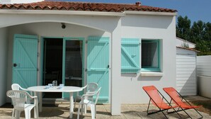 A patio area with a white table and chairs, a small covered seating area with a table, and two orange lounge chairs. - Cozy Vacation Home Near Beach with Private Garden and Parking (La Tranche-sur-Mer)
