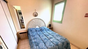 A bedroom with a bed, a nightstand, a mirror, a wall-mounted fan, and a window. - Cozy Vacation Home Near Beach with Private Garden and Parking (La Tranche-sur-Mer)