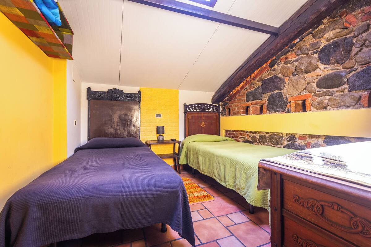 A room with two beds, a stone wall, and a yellow wall.