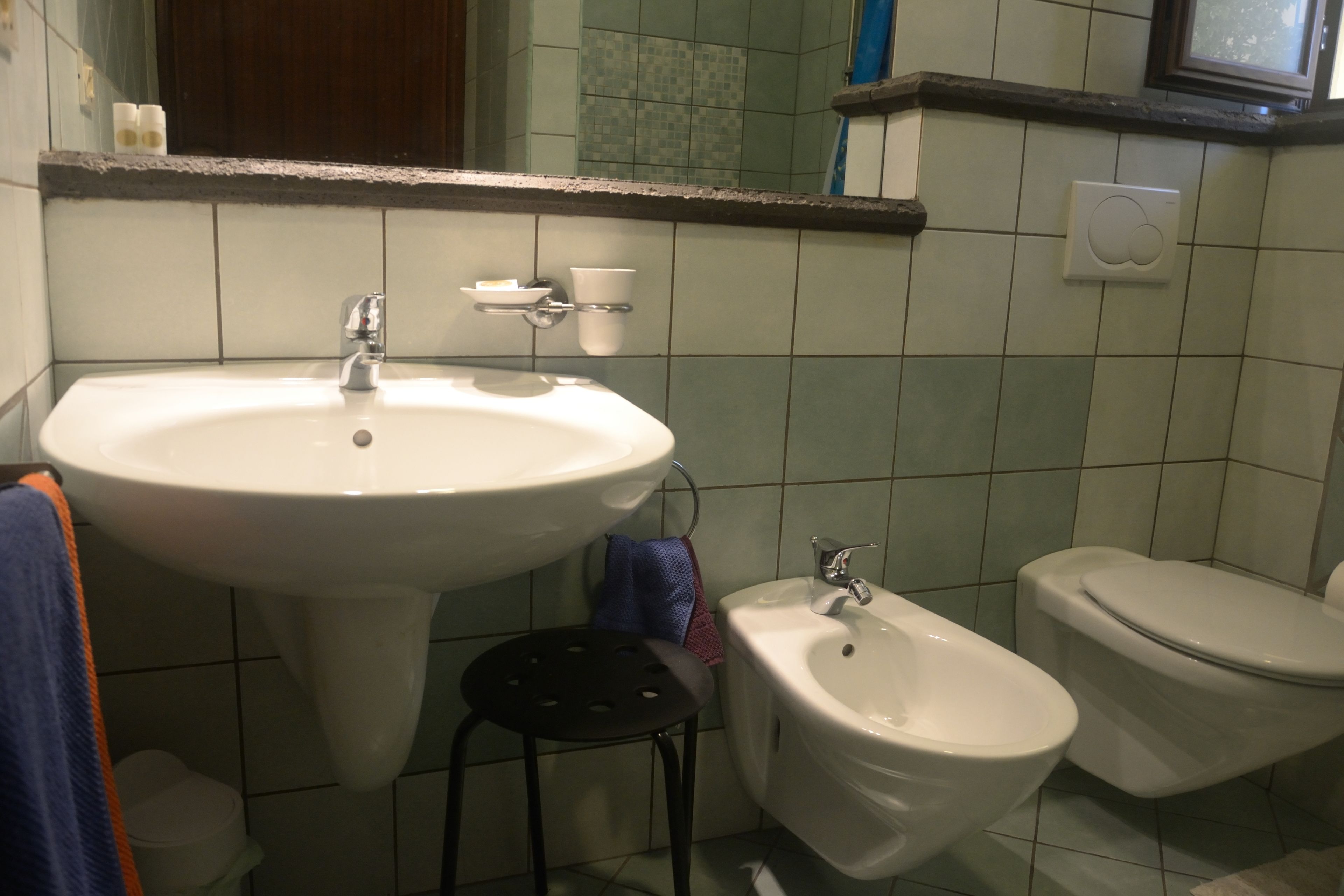 A bathroom with a sink, bidet, toilet, and a small stool.