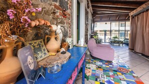 A rustic interior with a stone wall, a blue table with pottery, a colorful tiled floor, and a purple chair. - B&B Villa Felice (Giardini Naxos)