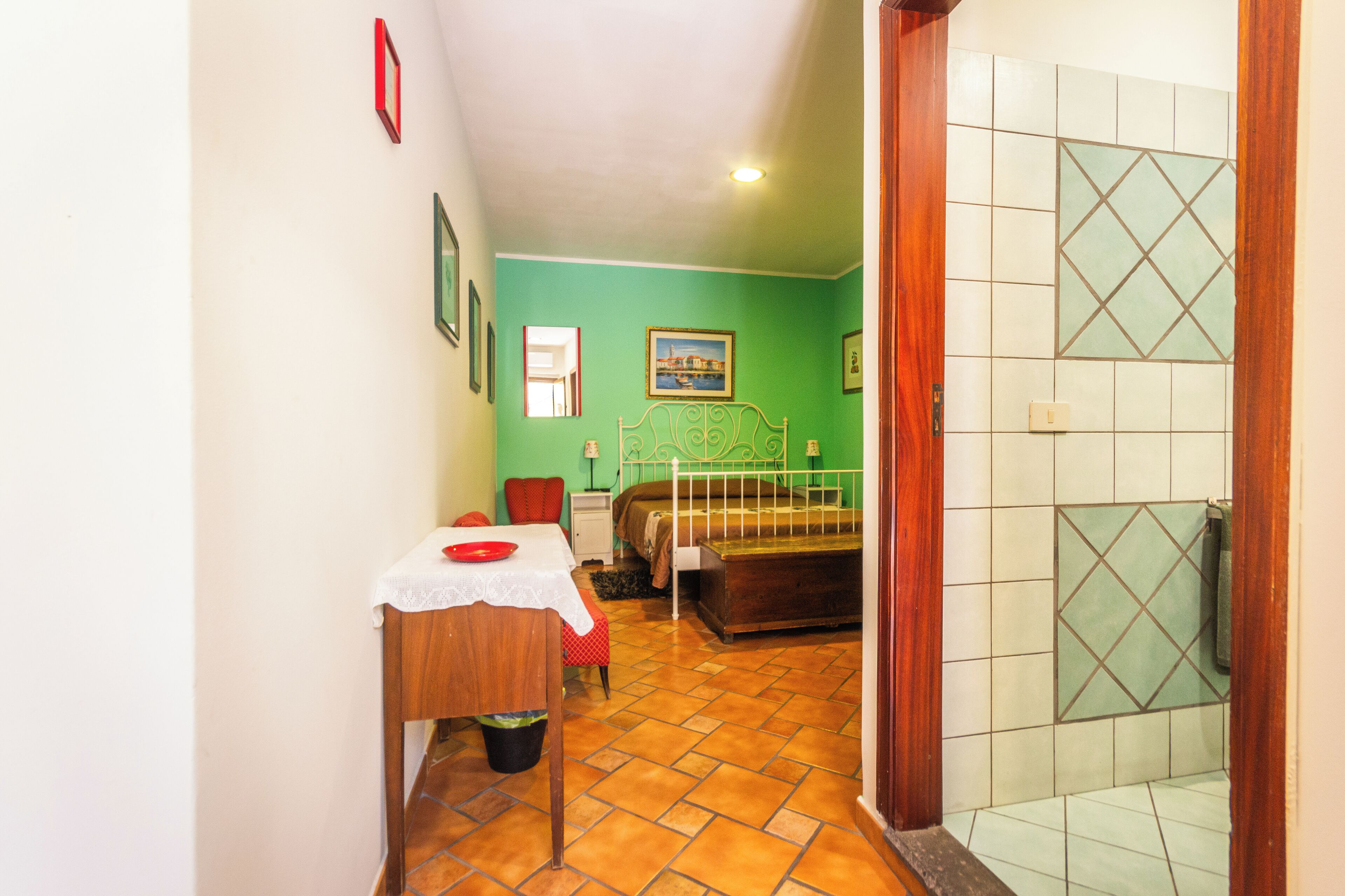 Un dormitorio con una cama, una mesita con una silla roja, un armario de madera y un baño con cabina de ducha.