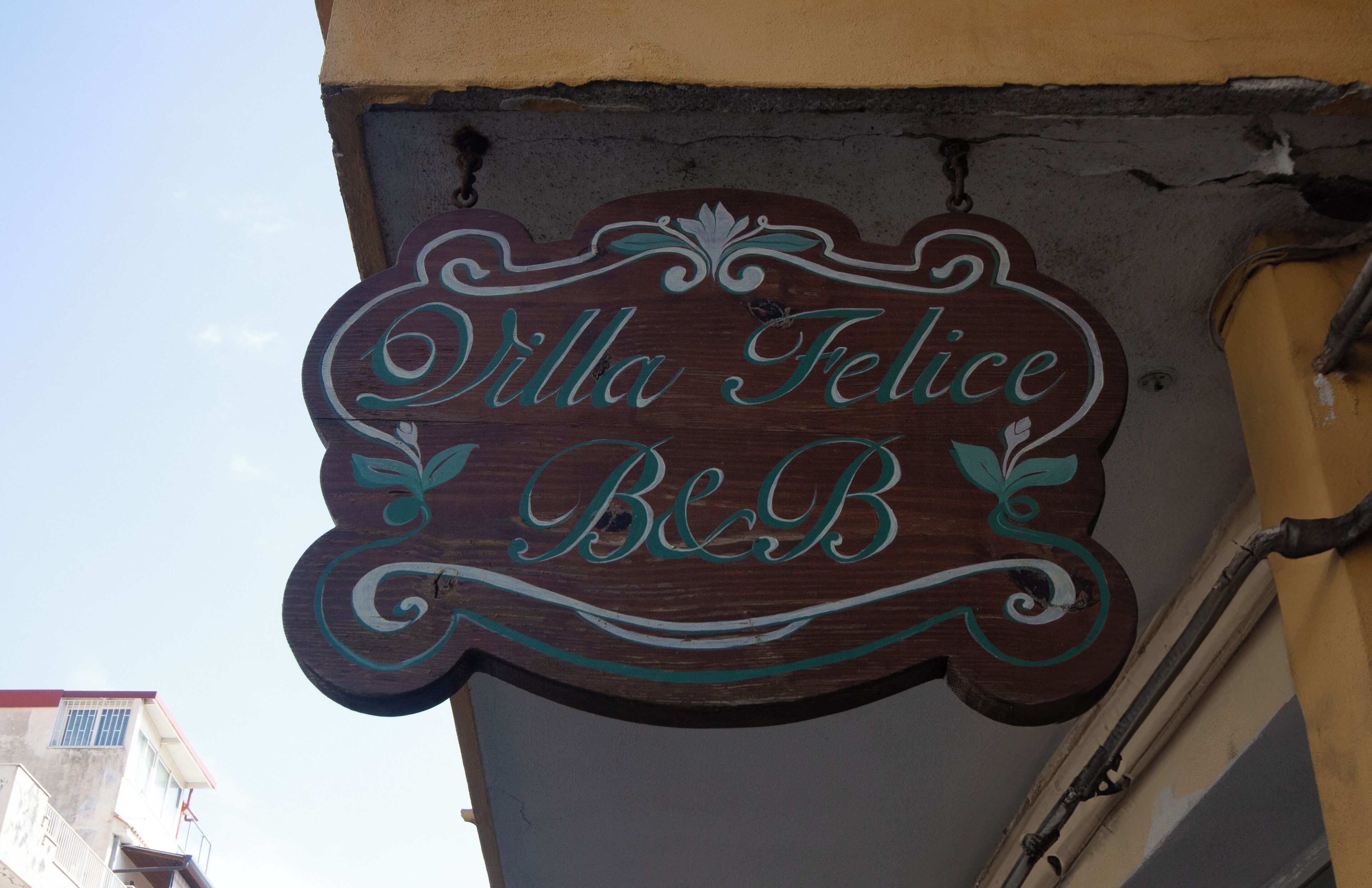Een houten bord met de naam 'Villa Felice B&B' in sierlijke letters.
