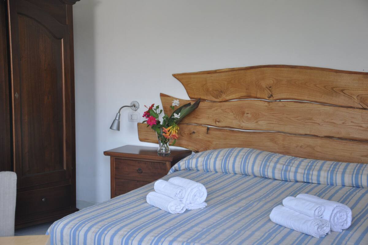 A neatly made bed with striped bedding, a wooden headboard, and rolled towels on the bed.