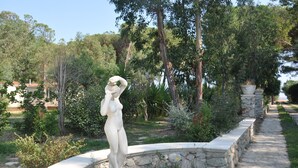 A statue of a woman in a garden with a stone pathway and trees. - Villaggio Borgo degli Ulivi (Sellia Marina)