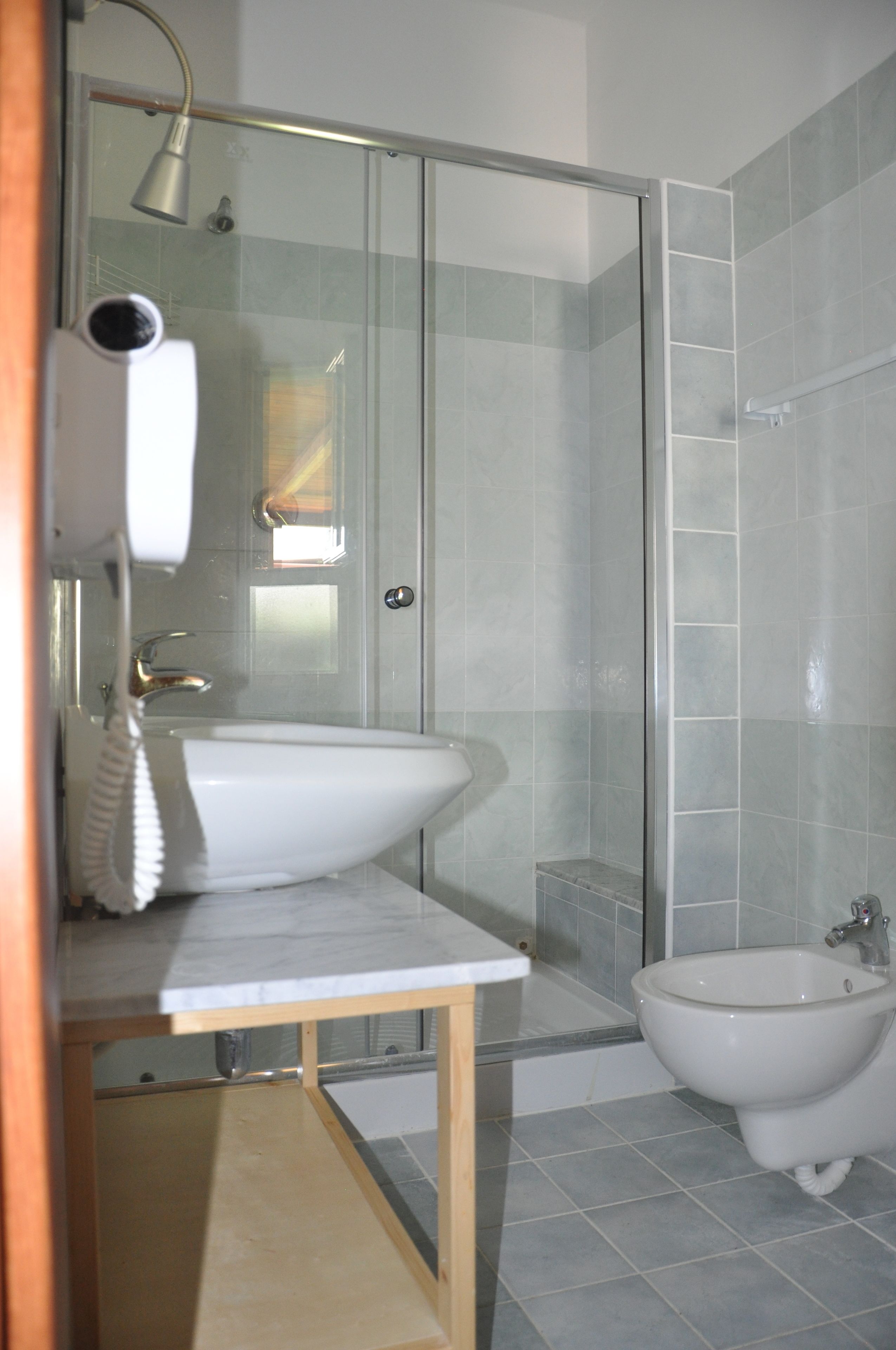 A bathroom with a glass shower enclosure, a sink, and a bidet.