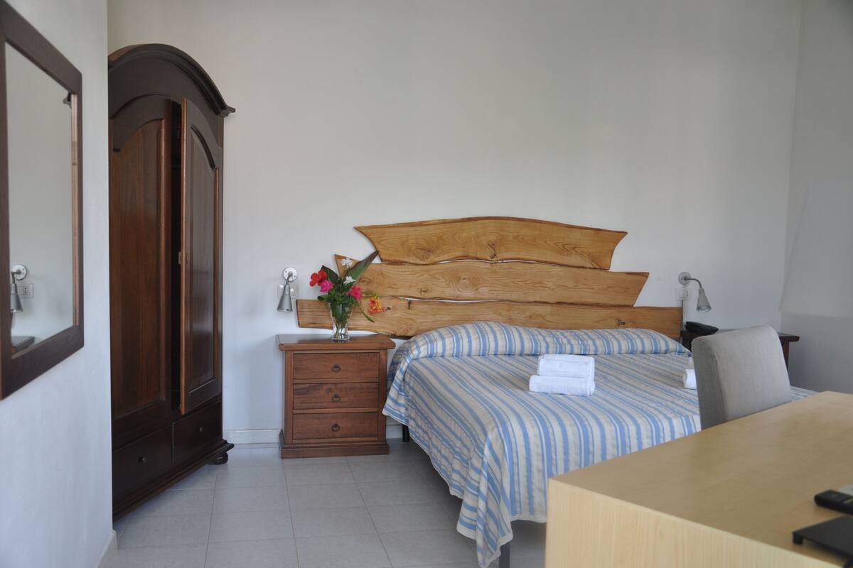 A bedroom with a wooden headboard, a bedside table with a lamp, a dresser, and a bed with striped bedding.