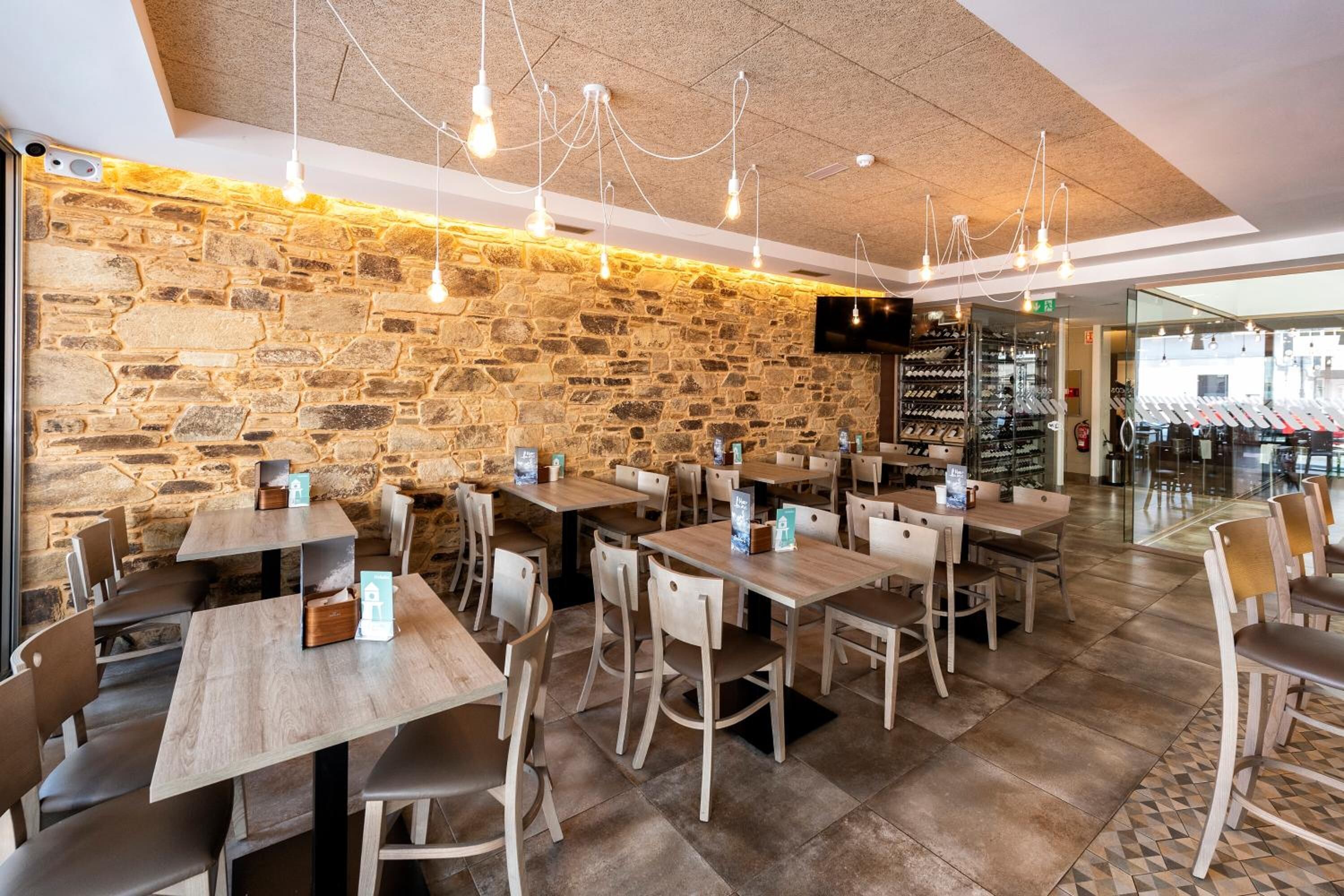 A restaurant with stone walls, wooden tables, and hanging light fixtures.