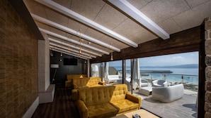 A modern interior with a sofa and a table, large windows with a view of the sea, and a wooden ceiling. - Apartamentos Vida Mar de Laxe (Laxe)