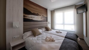 A hotel room with two beds, a large painting on the wall, a TV mounted on the wall, and a window providing natural light. - Apartamentos Vida Mar de Laxe (Laxe)