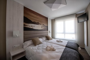 Habitación de hotel con dos camas, un cuadro grande en la pared, un televisor montado y una ventana con persianas.