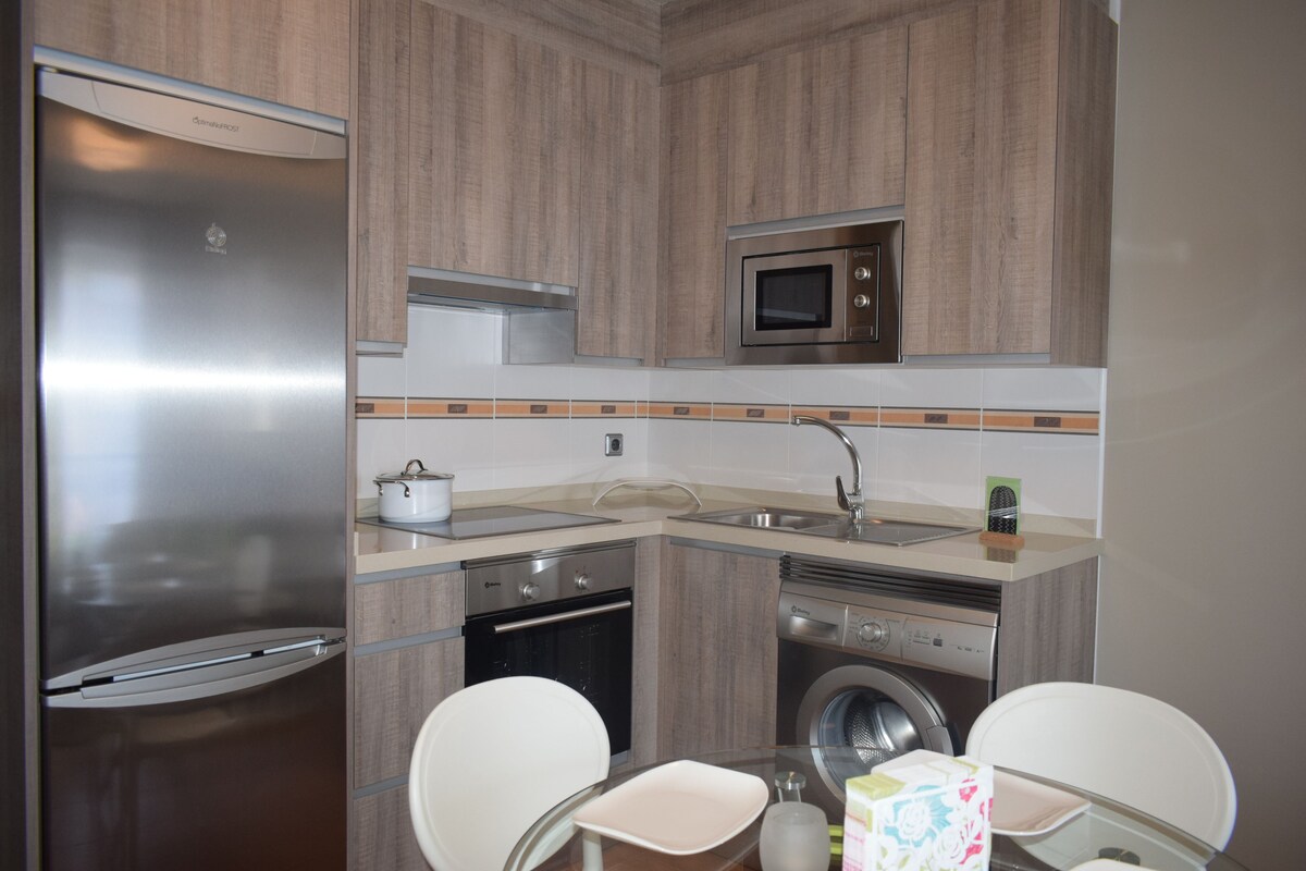 A compact kitchen with a refrigerator, microwave, oven, and washing machine.