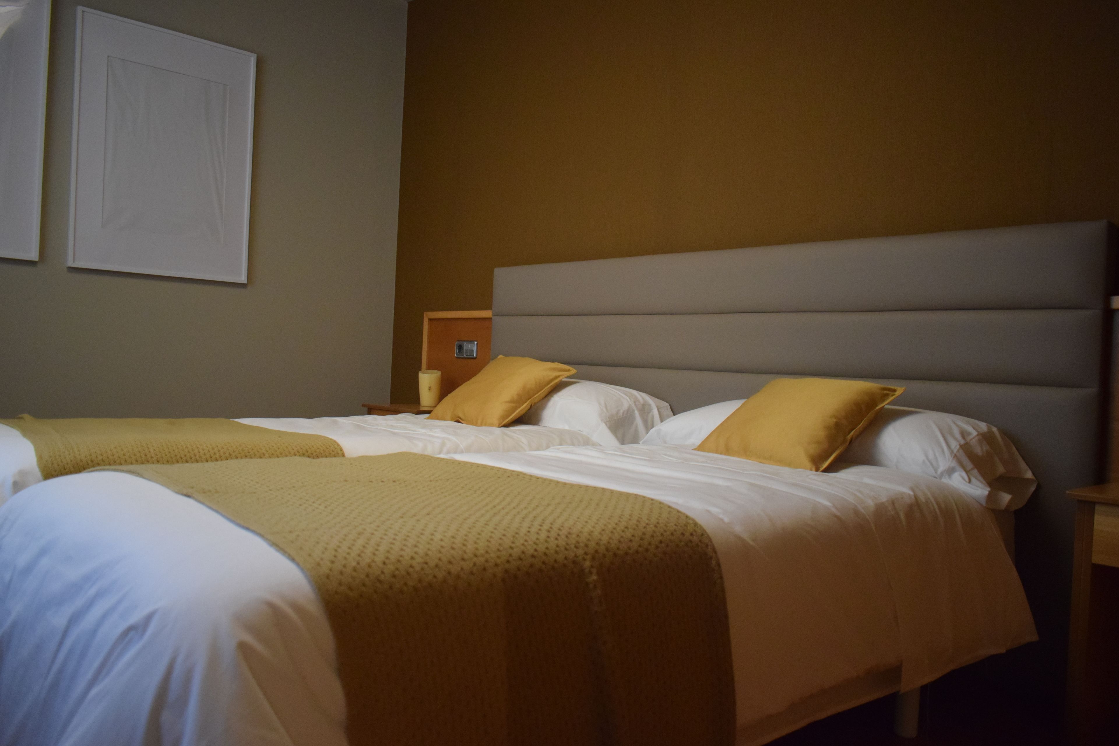 A hotel room with two beds, a headboard, and a bedside table with a lamp.