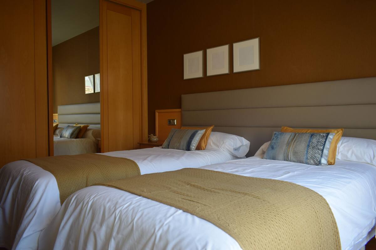 Habitación de hotel con dos camas, un armario de madera, una mesita de noche y un estante en la pared.