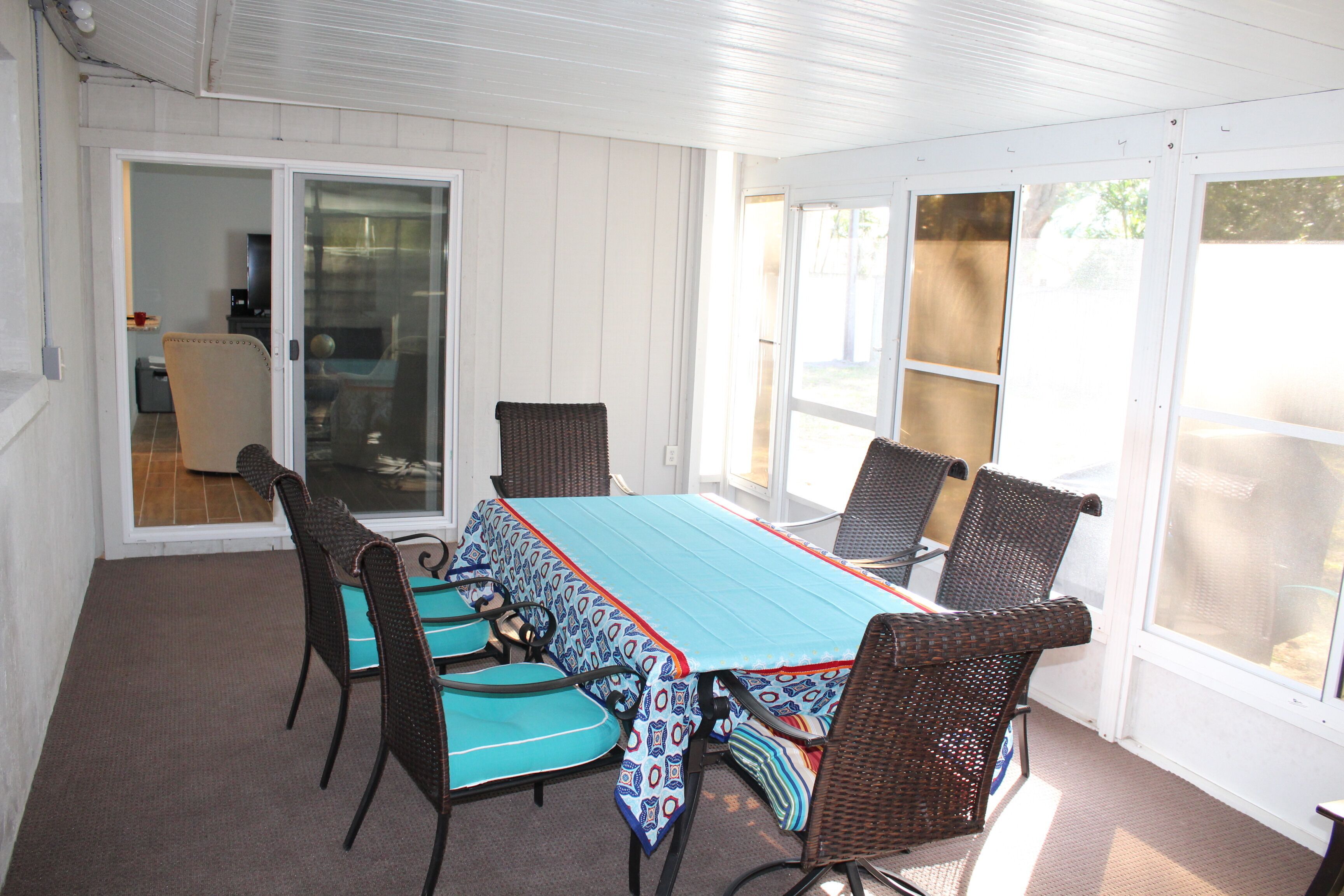 En overdækket terrasse med et bord og stole, en skydedør samt udsigt til naturen.