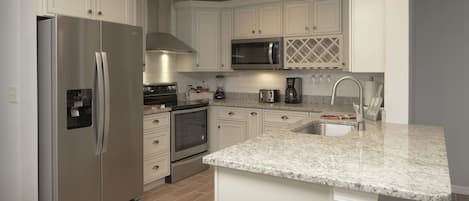 A modern kitchen with white cabinetry, stainless steel appliances, a granite countertop, and a built-in oven.