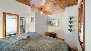 A bedroom with a wooden ceiling, a bed with a floral bedspread, a painting on the wall, and a potted plant shelf. - Vacation Cottage in Yonahlossee Resort (Boone)