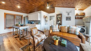 A cozy living room with a wooden ceiling, a sofa, a coffee table, and a dining area with stools. - Vacation Cottage in Yonahlossee Resort (Boone)