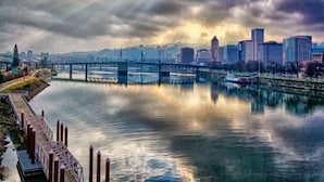 Un paisaje urbano con un río, un puente y edificios al fondo.