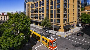 Un edificio moderno con fachada amarilla y varios pisos, con una línea de tranvía frente a él.