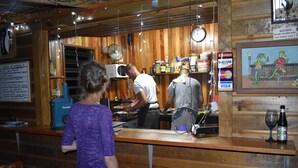 Un coin bar au décor rustique, avec des murs en bois, une horloge et un tableau affichant le menu.