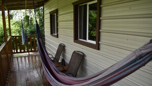 Une véranda avec un hamac, une balustrade en bois et deux chaises.