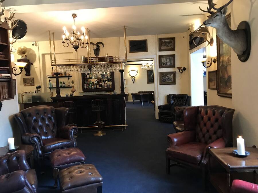 Un interior tradicional con sillones de cuero, una zona de bar con candelabro y monturas de animales.