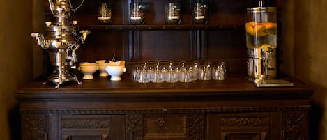 Una zona con barra de madera, máquina de café, frascos de especias y dispensador de fruta.