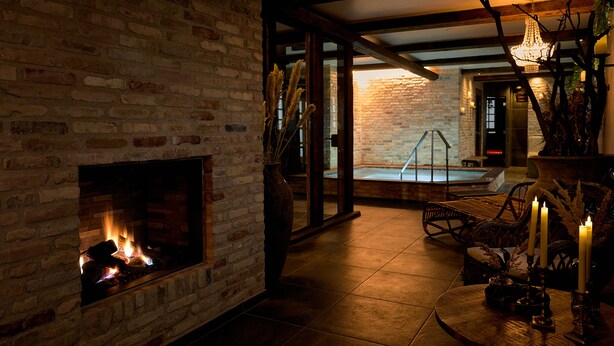 Una habitación acogedora con chimenea de ladrillo, puerta de vidrio que da a una zona de piscina y una mesa de madera con velas.