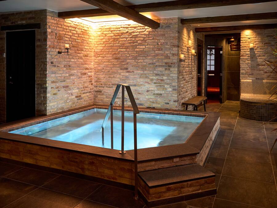 Een wellnessruimte met een jacuzzi, houten banken en een bakstenen muur.
