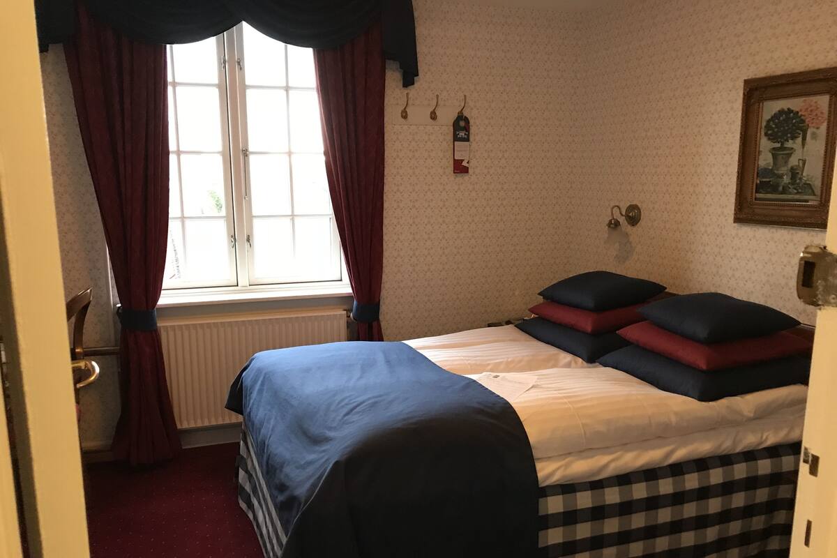 Un dormitorio con cama, un radiador, una ventana con cortinas, un reloj de pared y un cuadro enmarcado.