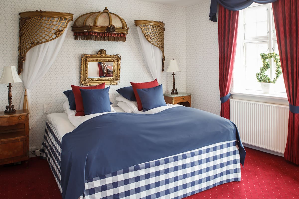 Un dormitorio con una cama grande, dos mesitas de noche, un espejo y una ventana con cortinas rojas.