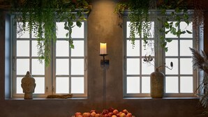 Una habitación con un ventanal grande, una vela en un soporte de pared, una mesa de madera y un cuenco de fruta.