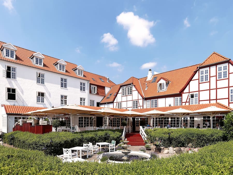 Un hotel de estilo europeo tradicional con varias edificaciones, un patio central con asientos y una fuente.